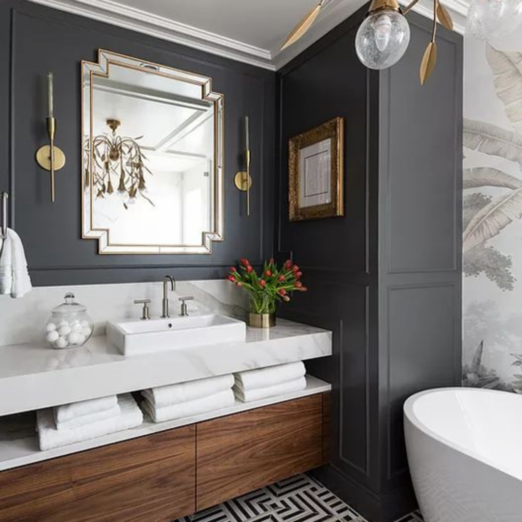 Professionally decorated bathroom with wallpaper and dark builtin units.  Brass sconces flank a mirror above the custom wood and marble vanity. 