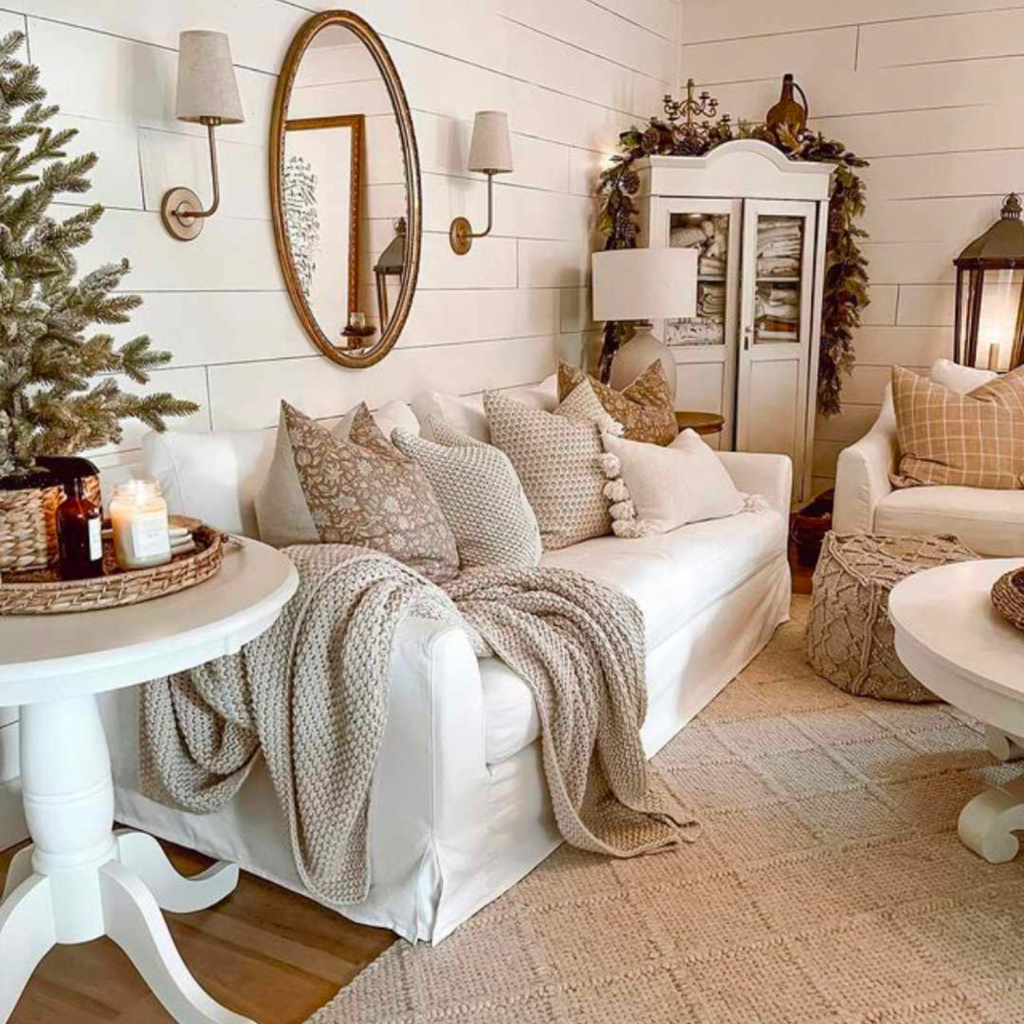 Boho interior design style living room combines organic looking elements in mostly nude and white color palette.  White sofa includes a textured throw and ottoman.  Surrounding the upholstery is warm looking case goods. 