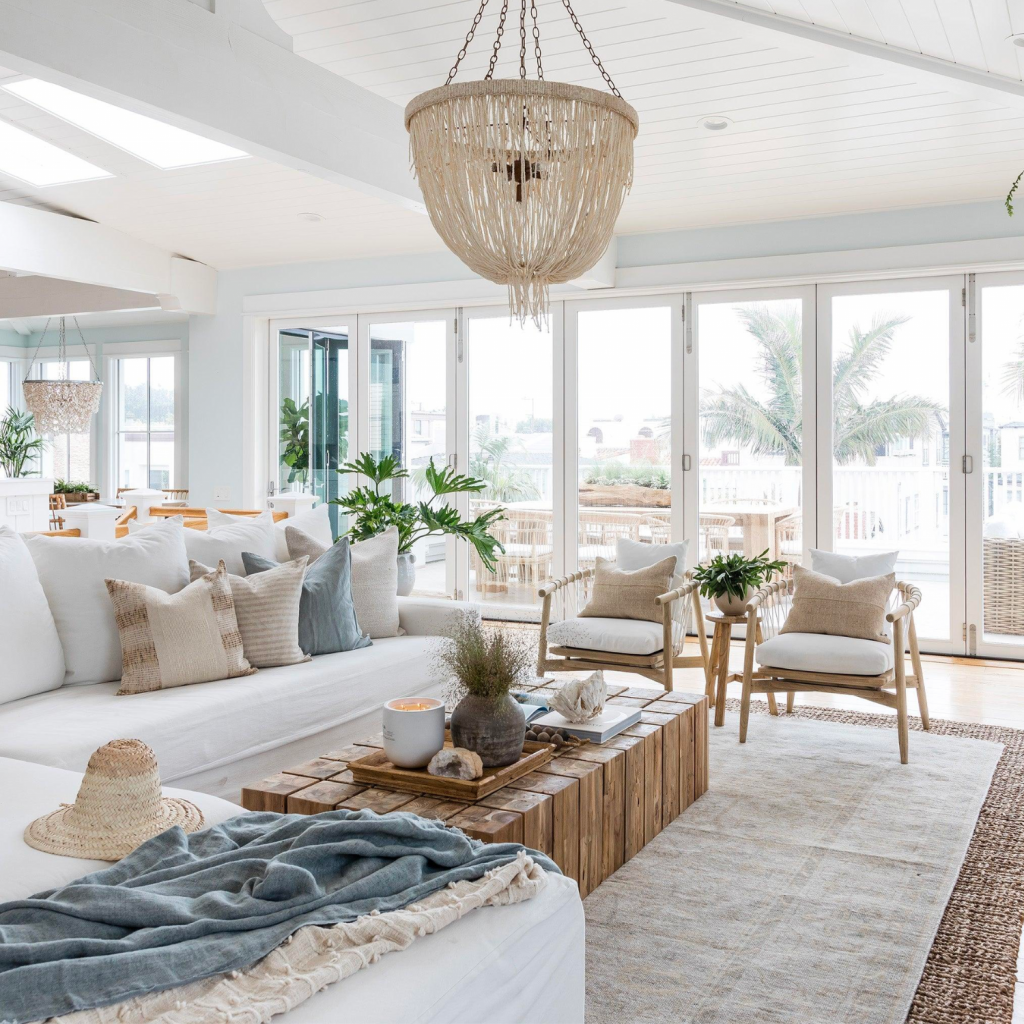 Coastal interior design style living room includes an all white color palette with beachy blue tones.  Seagrass elements in the rug are present, with a wood coffee table.