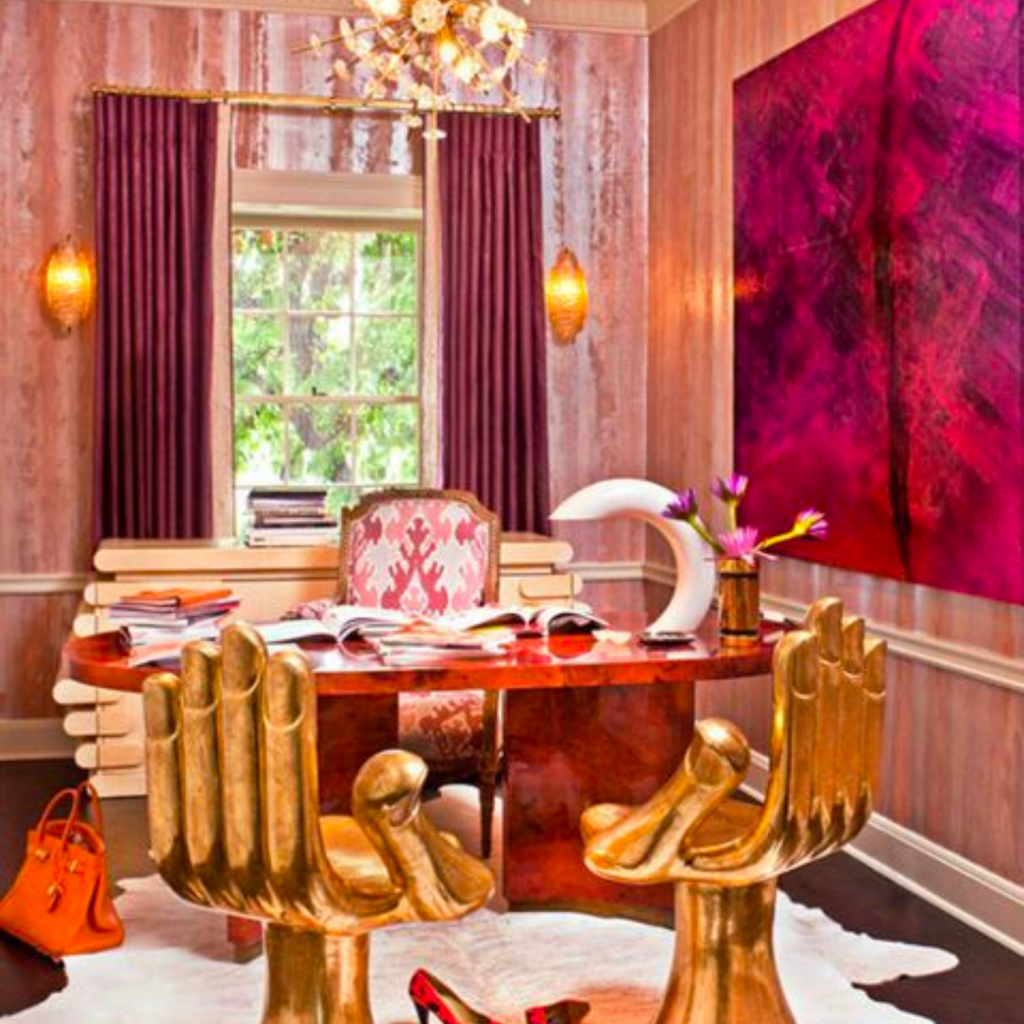 Eclectic interior design style office with vivid, bold colors on the wall and drapery.  A red office desk is pared with brass chairs in the shape of a large hand. 